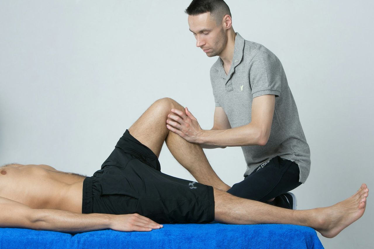 Ein Physiotherapeut untersucht das Knie eines Patienten, der auf einem blauen Behandlungstisch liegt.