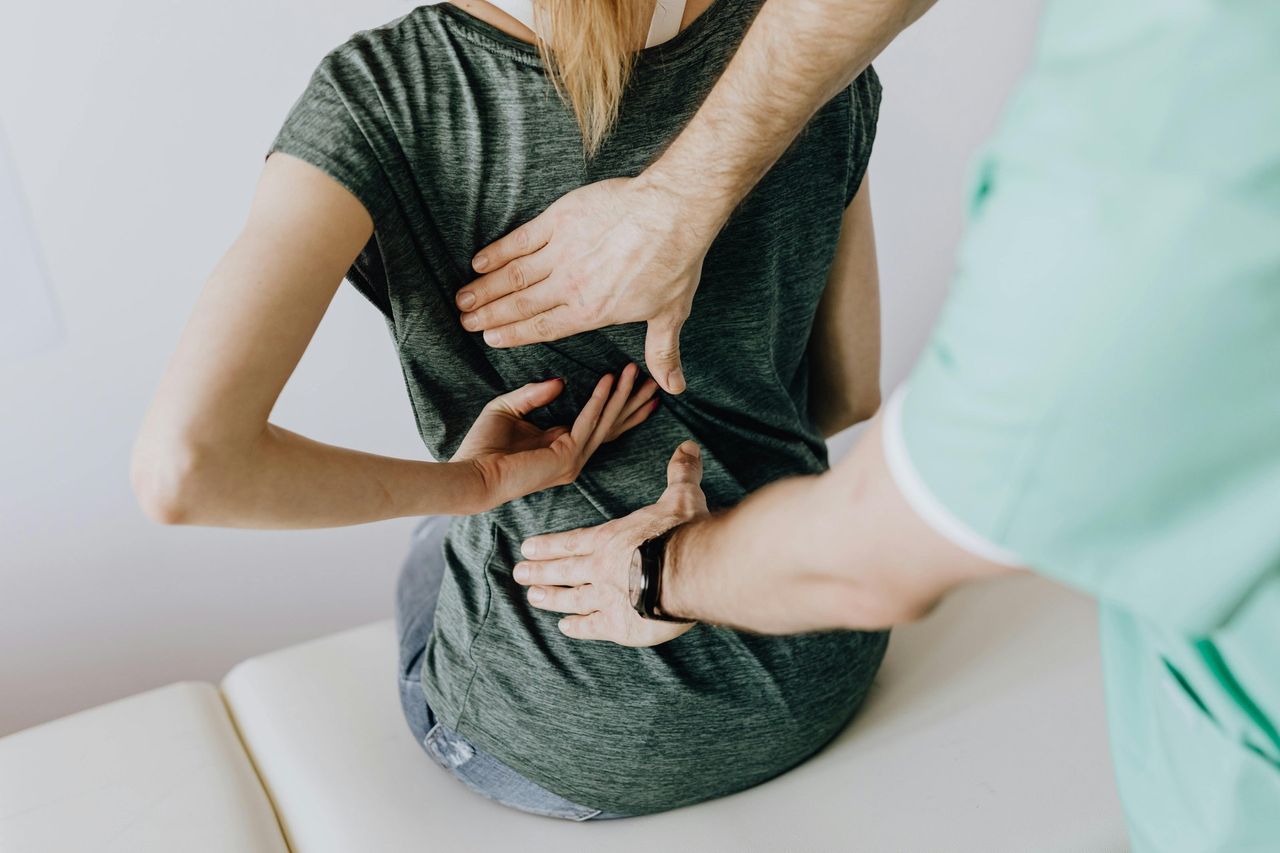 Triggerpunktmassage: Ein Physiotherapeut ertastet Verspannungspunkte im Rücken einer sitzenden Frau.
